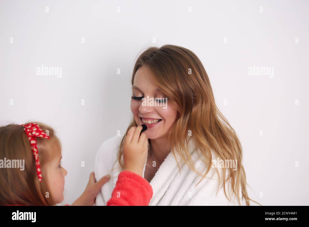 Mère et fille sont assises sur le lit dans la chambre. Famille heureuse et aimante. Mère et fille font les cheveux, maquillage Banque D'Images