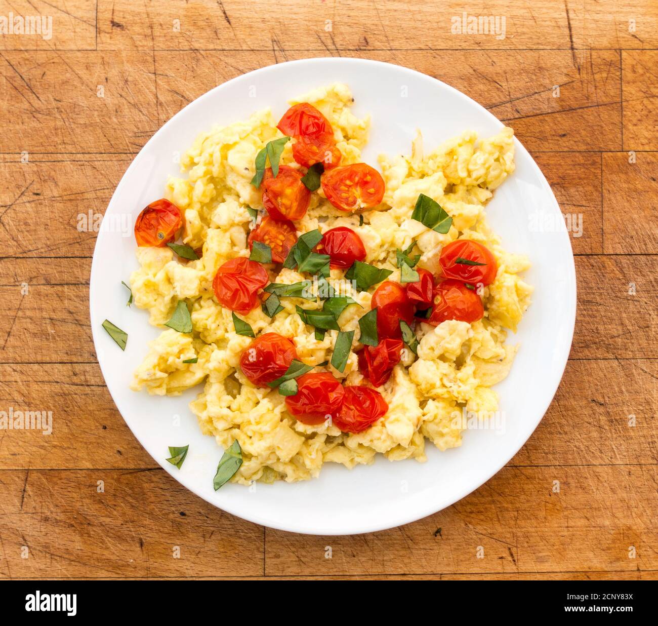 Une assiette d'œufs brouillés, de tomates grillées et de basilic fraîchement coupé sur fond de bois vieilli. Banque D'Images