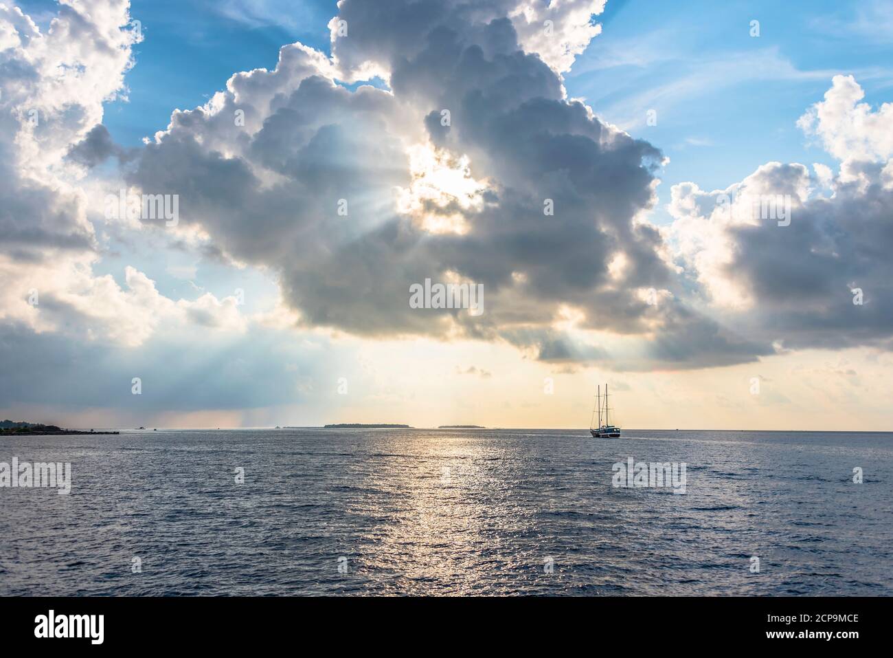 Le soleil brille à travers un pittoresque nuages sur l'Indien océan avec les îles Maldives à l'horizon et la silhouette d'un navire avec des mâts Banque D'Images