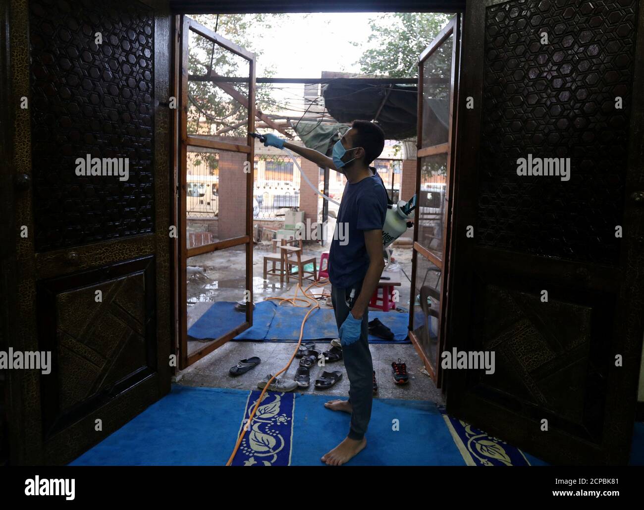 Un volontaire portant un masque facial vaporise du désinfectant à l'intérieur d'une mosquée alors qu'il est prêt à la prière après avoir été rouvert, après l'épidémie de coronavirus (COVID-19), au Caire, en Égypte, le 26 juin 2020. REUTERS/Mohamed Abd El Ghany Banque D'Images