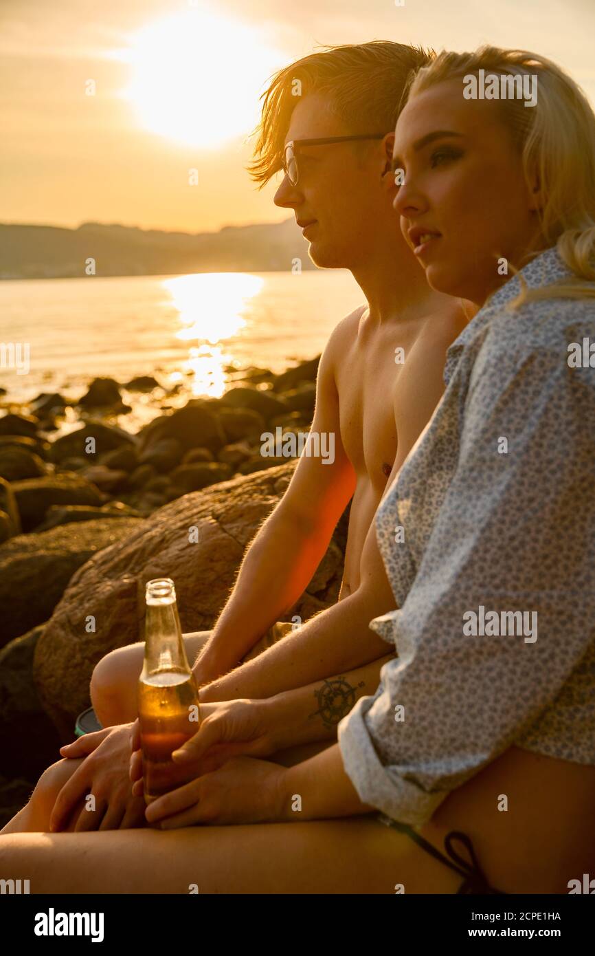 Couple et de boire une bière sur la plage au coucher du soleil Banque D'Images