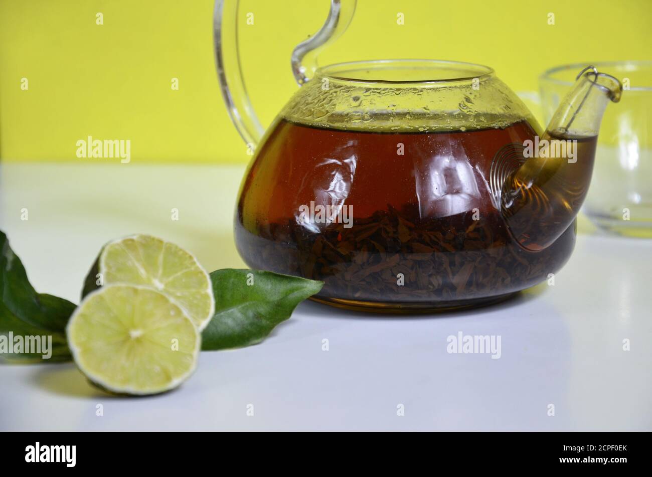 Théière transparente avec thé noir, préparation de thé sec sur la table, tranches de bergamote ou citron ou lime sur fond blanc Banque D'Images