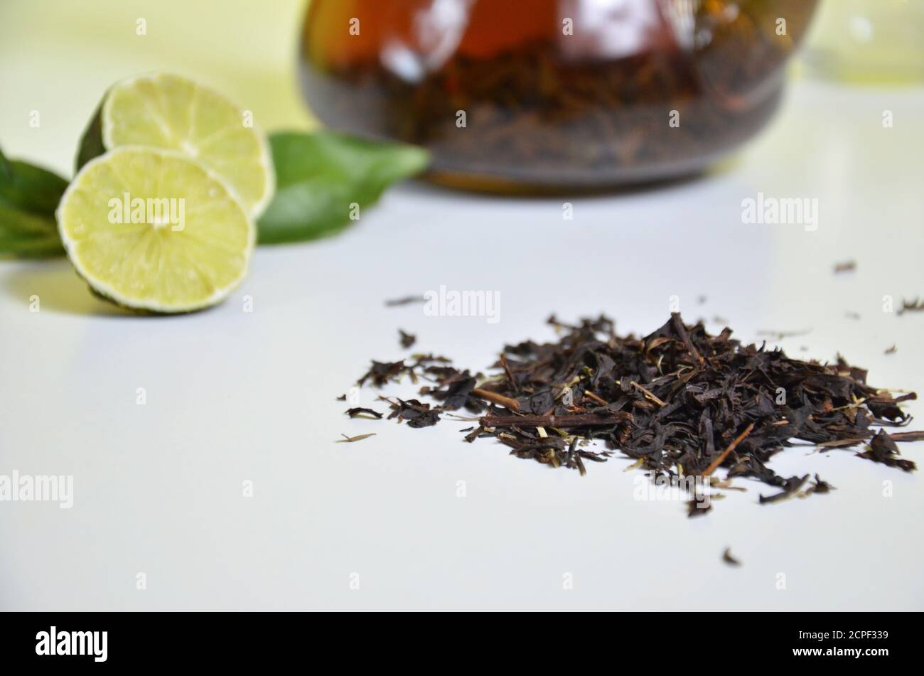 Théière transparente avec thé noir, préparation de thé sec sur la table, tranches de bergamote ou citron ou lime sur fond blanc Banque D'Images
