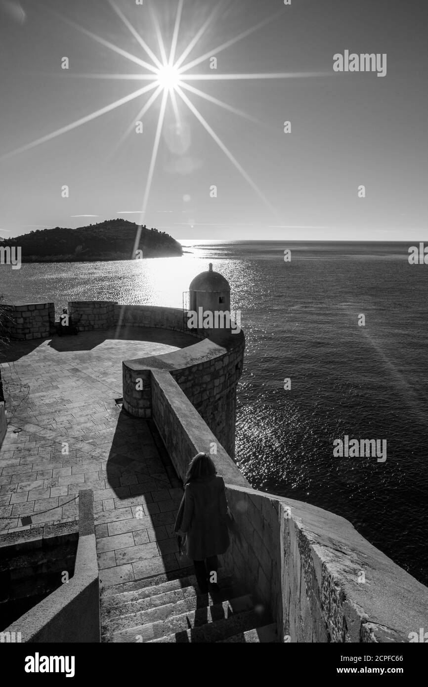 Rue forteresse scène noire et blanche, ciel clair jour. Diffraction des rayons du soleil, silhouette féminine vue d'hiver de la vieille ville méditerranéenne de Dubrovnik, célèbre voyage européen et destination historique, Croatie Banque D'Images