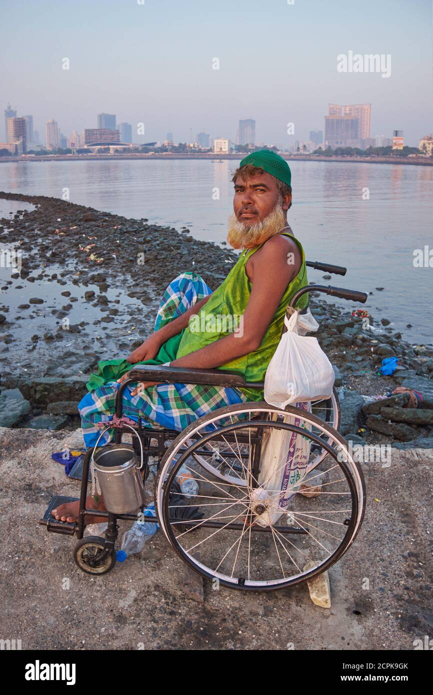 Un mendiant musulman en fauteuil roulant, assis dans son fauteuil roulant sur la passerelle menant à la mosquée Haji Ali et Durgah, construite dans la baie de Worli, Mumbai, Inde Banque D'Images