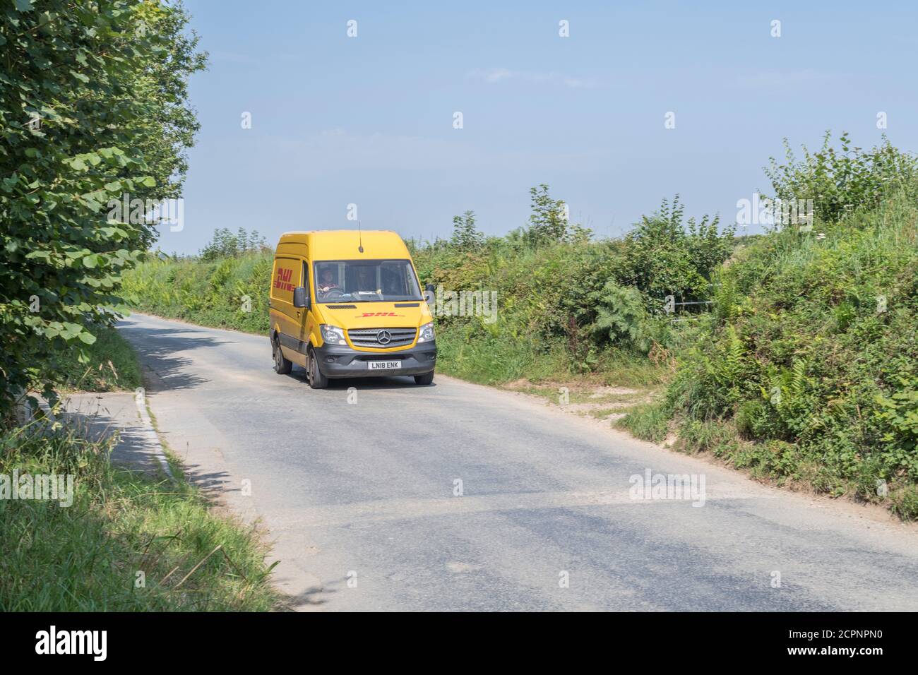 Minibus de livraison jaune DHL (Mercedes Sprinter) sur une route rurale Cornish. Pour les services de livraison rurale au Royaume-Uni, les livraisons de colis, les services de messagerie. Banque D'Images