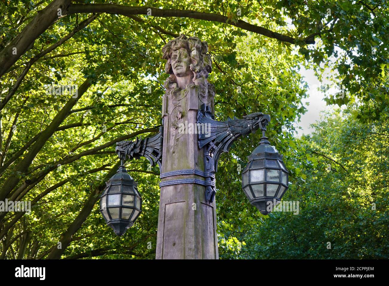 Ancienne lanterne en pierre sur le boulevard commerçant Königsallee, dans le centre-ville de Düsseldorf, entourée de vieux arbres verts. Banque D'Images
