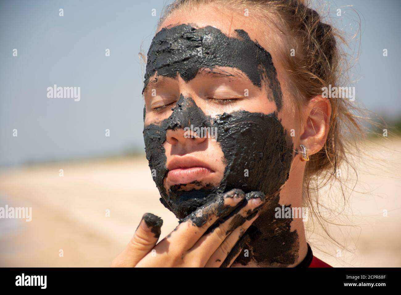 Jeune belle fille avec un masque de boue magnétique gris sur son visage sur un fond blanc Banque D'Images