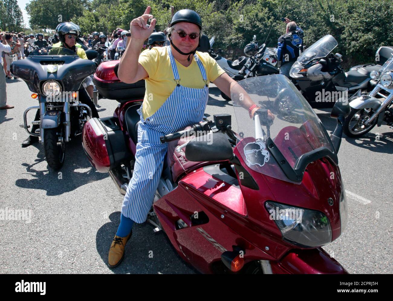 Un homme habillé comme acteur et comique français, Michel Colucci, appelé ' Coluche', se fait l'effet de vagues comme des centaines de motocyclistes se  rassemblent sur la route, où il y a trente