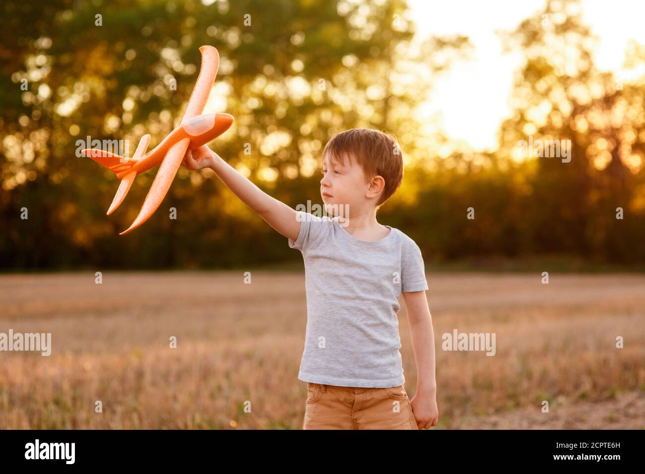Un enfant heureux court avec un avion jouet sur un fond de coucher de soleil sur un champ. Le concept d'une famille heureuse. Rêves d'enfance Banque D'Images