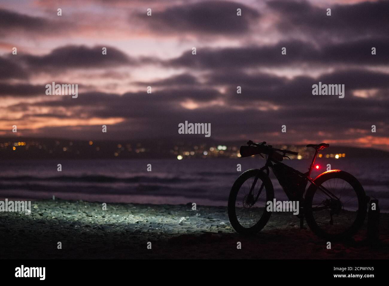 Vélo avec lumières sur la plage après le coucher du soleil Banque D'Images