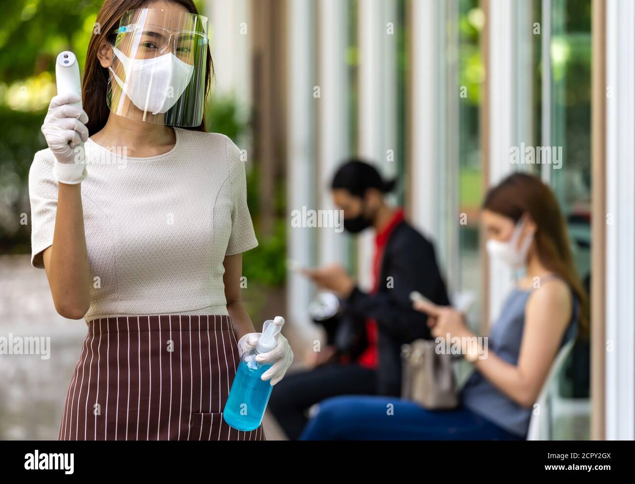 Portrait attrayant serveuse asiatique porter un masque facial et un thermomètre avec protection et gel désinfectant à base d'alcool avec fond de client de distanciation sociale Banque D'Images