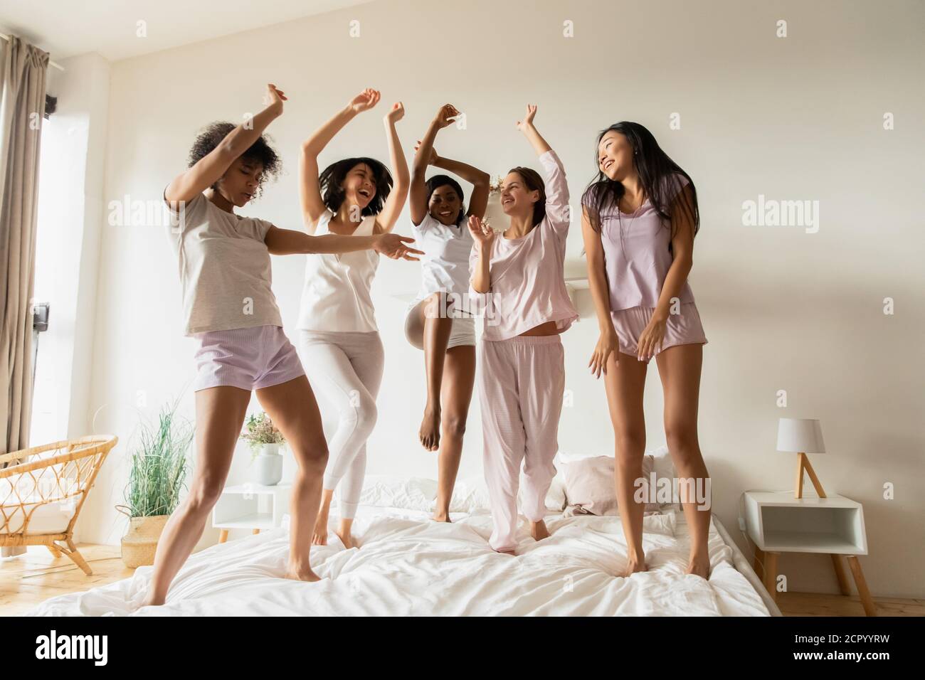 Joyeux jeunes femmes multiraciales en pyjama sautant sur le lit. Banque D'Images