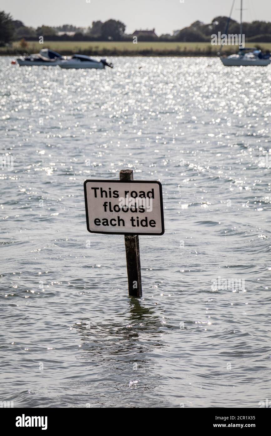 Un panneau indiquant « cette route inonde chaque marée » partiellement submergé à marée haute dans le village historique de Bosham, West Sussex, Royaume-Uni. Banque D'Images