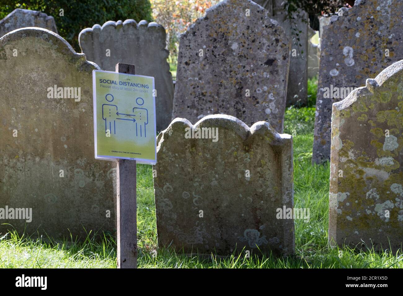 Pierres de tête de cimetière d'église regroupées étroitement avec un coronavirus social de distancement avis. Banque D'Images