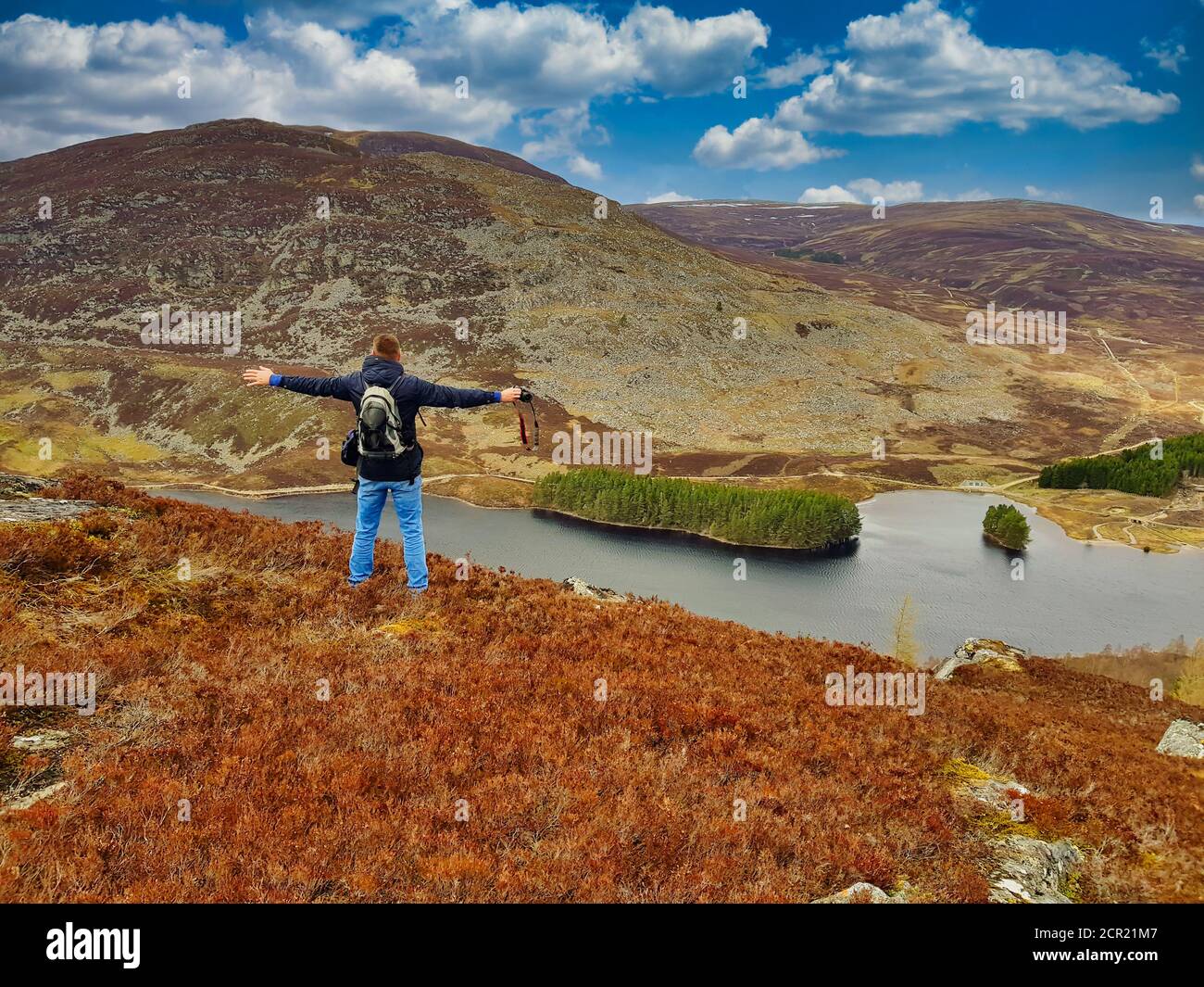 Un homme levant les mains ouvre les bras. Explorez la montagne des montagnes, homme face à un lac dans les montagnes écossaises. Banque D'Images