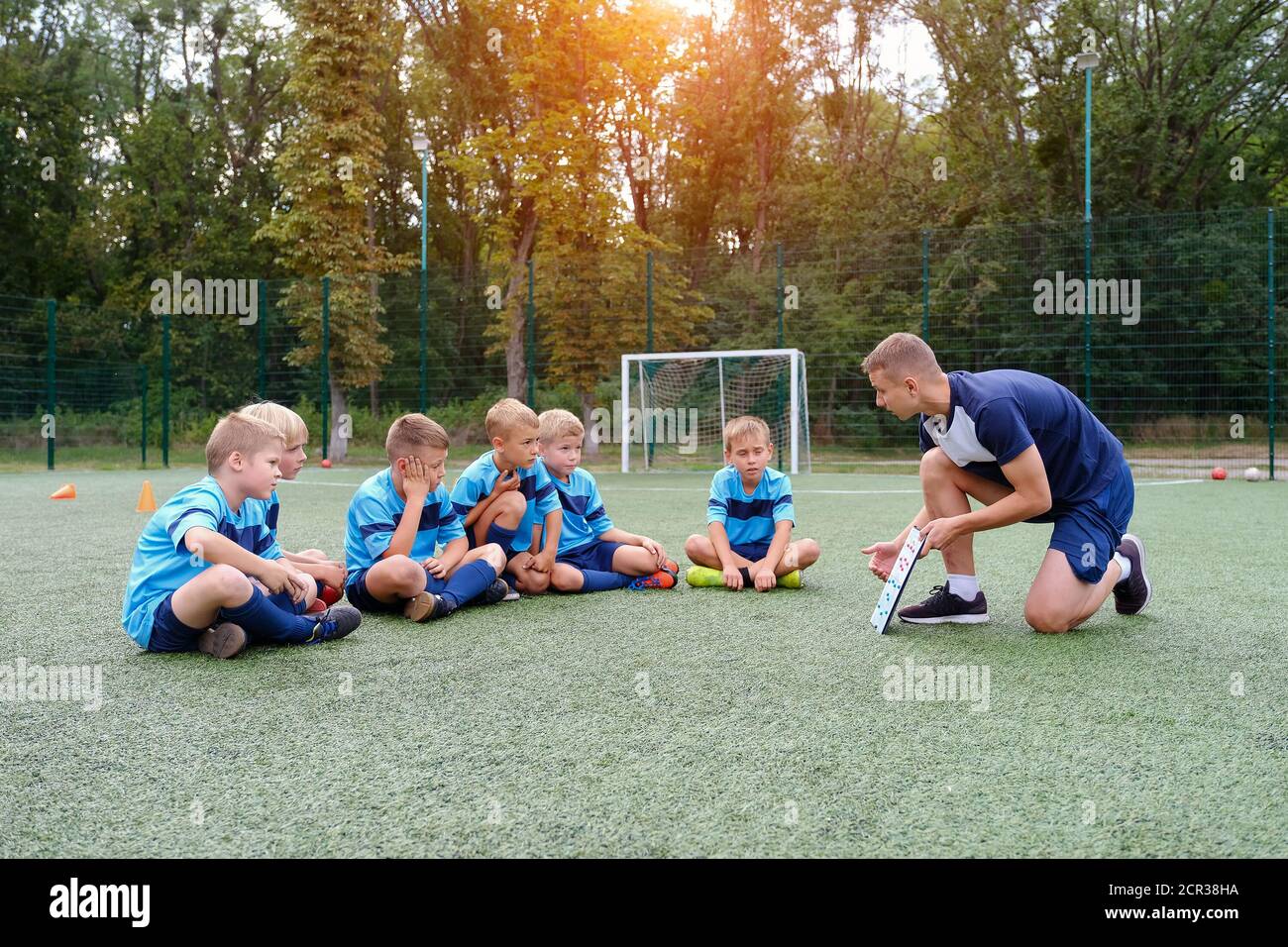 Un jeune entraîneur avec presse-papiers enseigne la stratégie des enfants sur le terrain de football. Banque D'Images