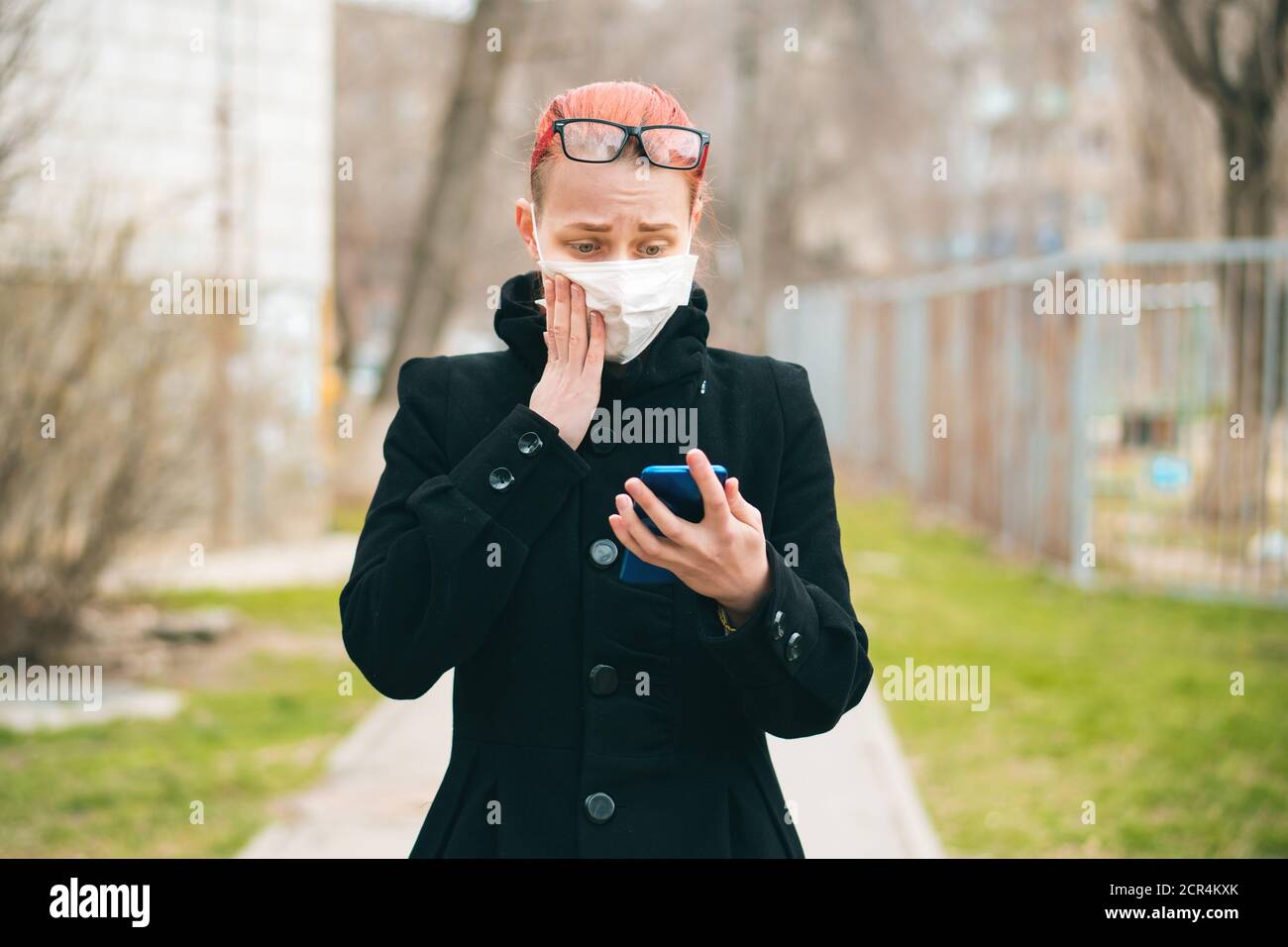 Fille dans le masque regarde le téléphone et lit des nouvelles sur le coronavirus. Concept de protection contre les épidémies et les virus. Banque D'Images