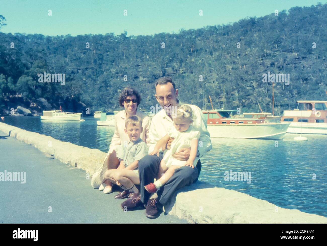 Bombbin Head, Sydney Australie 1965 : avec de beaux bateaux à coque en bois amarrés en arrière-plan, une jeune famille australienne pose pour une photo au bord de l'eau à Bobbin Head, dans le parc national de Kurant-Gai, Sydney, Australie Banque D'Images
