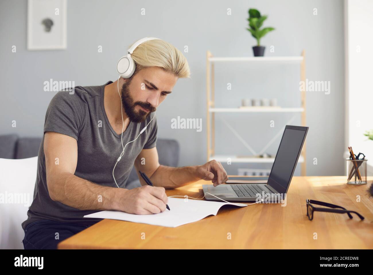 Formation en ligne. Un jeune homme assis à une table à la maison à l'aide d'un ordinateur portable et d'un appel vidéo pour écouter une leçon en ligne. Banque D'Images