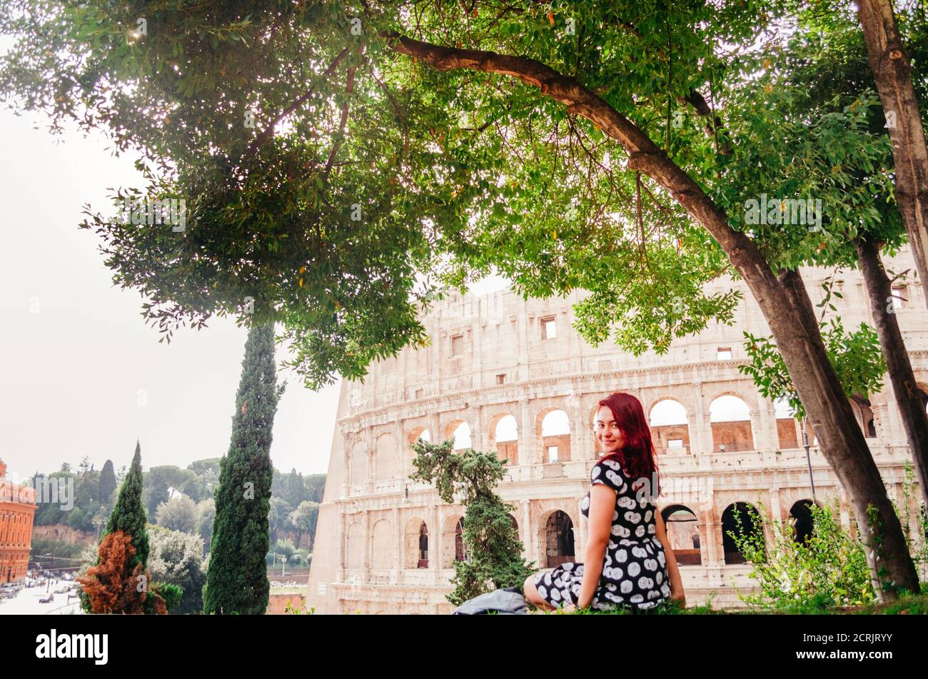 Rome, Italie - UNE jeune femme brésilienne adulte à tête rouge dans ses années 20 regardant de nouveau la caméra avec le Colisée en arrière-plan pendant l'après-midi. Banque D'Images