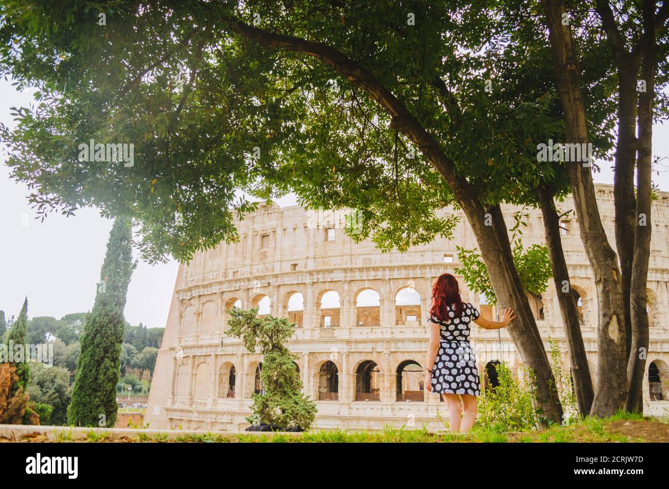 Rome, Italie - UNE jeune femme brésilienne adulte à tête rouge dans ses années 20s debout et regardant dans le Colisée pris dans un parc pendant l'après-midi. Banque D'Images