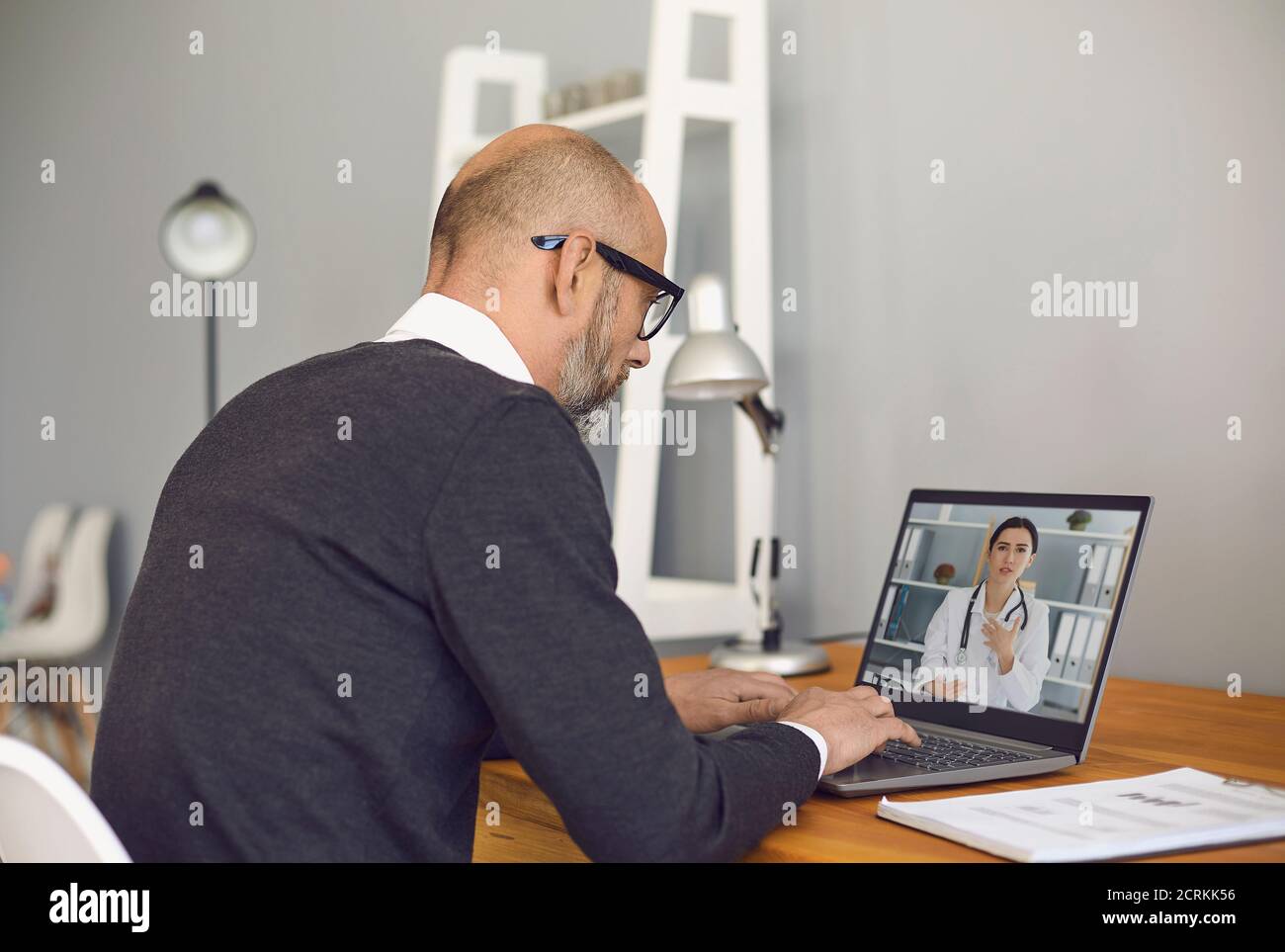 Médecin en ligne. Homme senior parlant à un médecin à l'aide d'une caméra vidéo portable d'appel vidéo, assis à une table à la maison. Banque D'Images