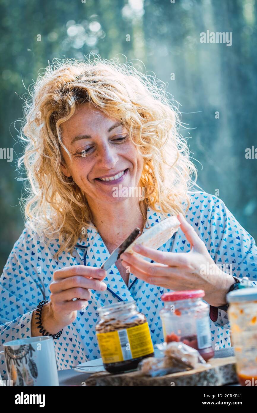 Blonde jeune femme mûre en pyjama à la maison au petit déjeuner préparer un toast. Banque D'Images