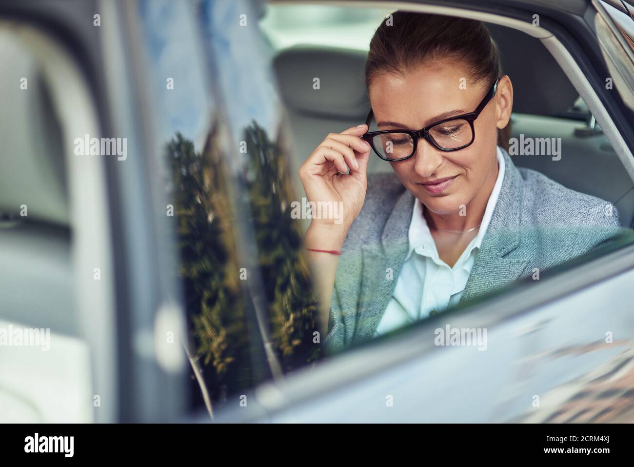 Belle femme d'affaires d'âge moyen en ajustant ses lunettes pendant qu'elle est assise sur le siège arrière en taxi Banque D'Images