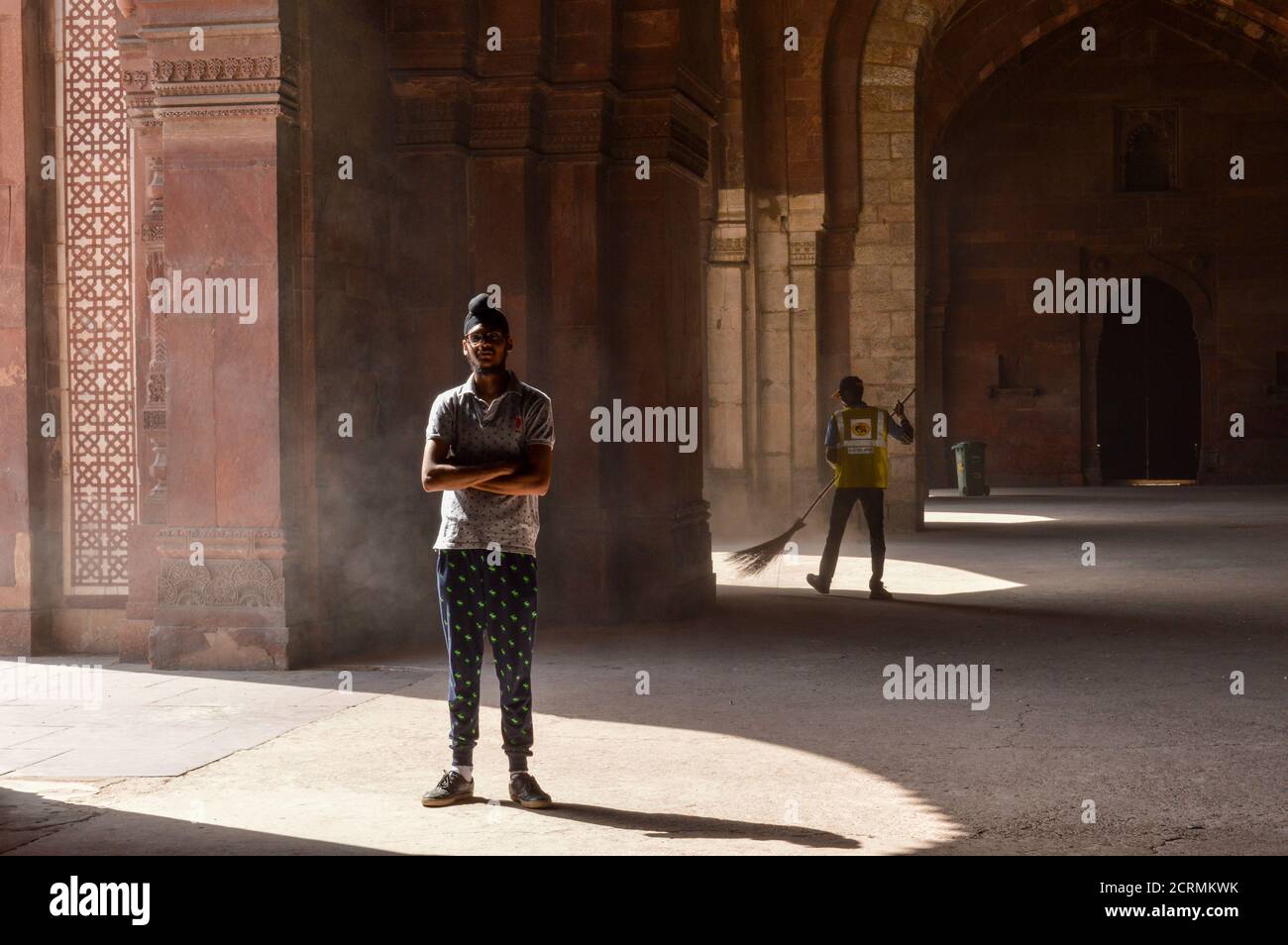 Un garçon indien qui pose pour une séance photo de mode à l'intérieur du vieux fort et un employé de l'ASI qui nettoie la zone. Banque D'Images