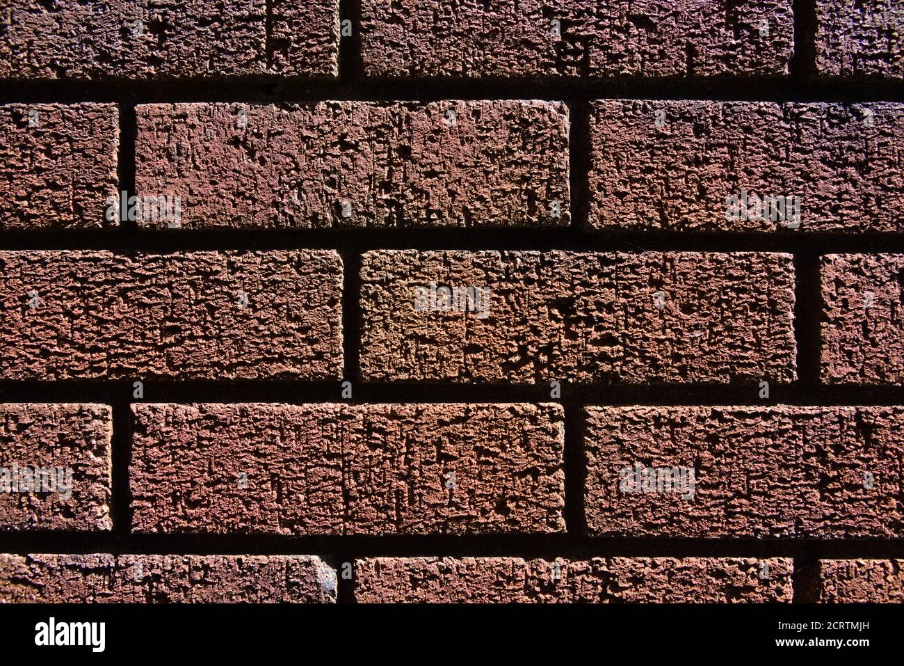 2 - texture abstraite gros plan d'un mur de briques rouges ombres et lumières vives font l'image contrastée. Grain fin et structure visibles. Horizontale. Banque D'Images