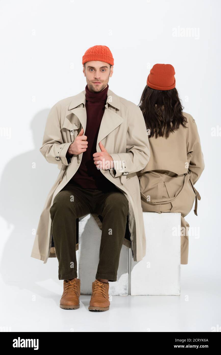 homme élégant en bonnet beanie touchant le trench coat près de la femme  assis sur blanc Photo Stock - Alamy