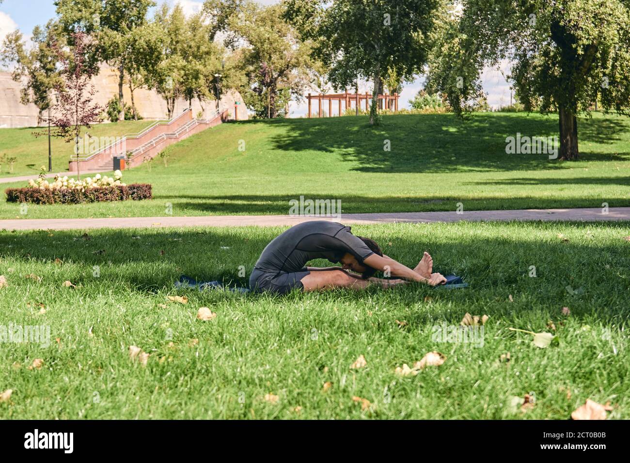 Jeune homme sportif en sport faisant du yoga dans le parc. Pratiquez l'asana à l'extérieur. Les personnes qui s'étirent sur l'herbe verte avec un tapis de yoga. Fitness Banque D'Images
