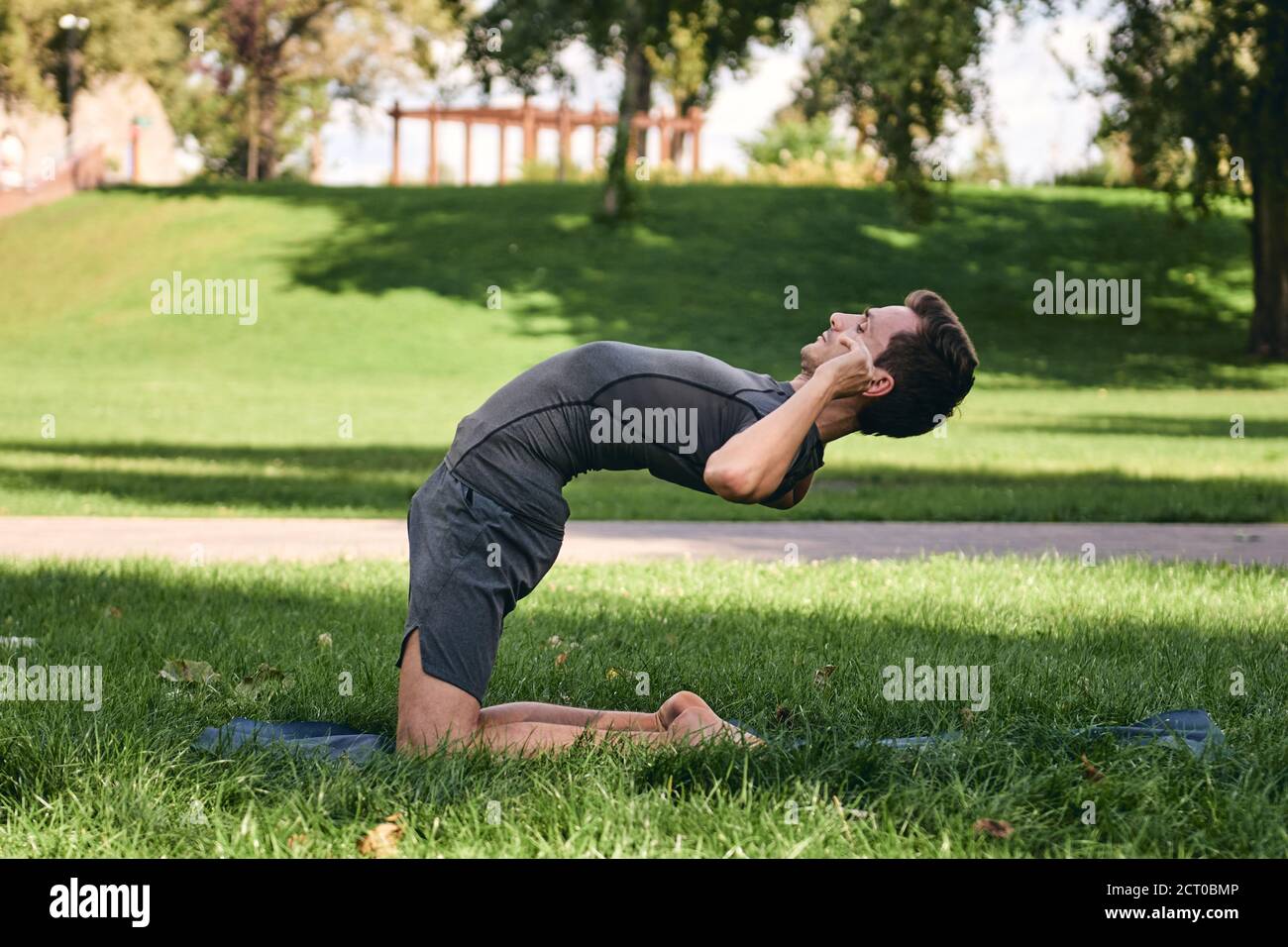 Jeune homme sportif en sport faisant du yoga dans le parc. Pratiquez le kapotasana asana à l'extérieur. Les personnes qui s'étirent sur l'herbe verte avec un tapis de yoga Banque D'Images