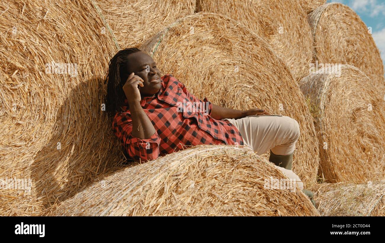 Gros plan, fermier noir africain assis sur la botte de foin et d'avoir un appel téléphonique. Photo de haute qualité Banque D'Images