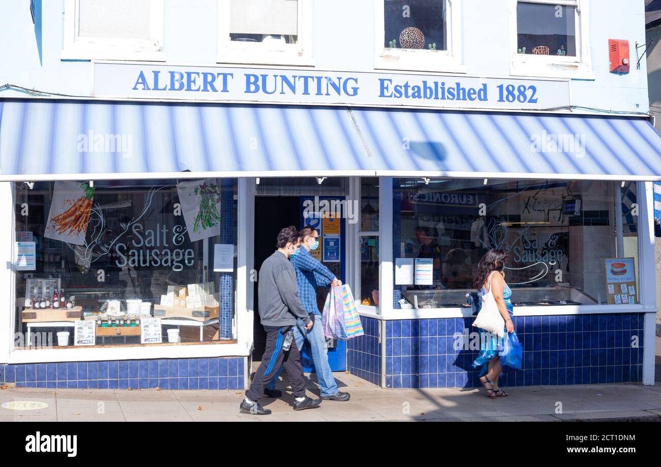 Vue sur la rue de deux hommes et d'une femme d'âge mixte marchant le long de la façade du magasin Salt & Sausage Butchers, Maldon, Essex, Royaume-Uni Banque D'Images