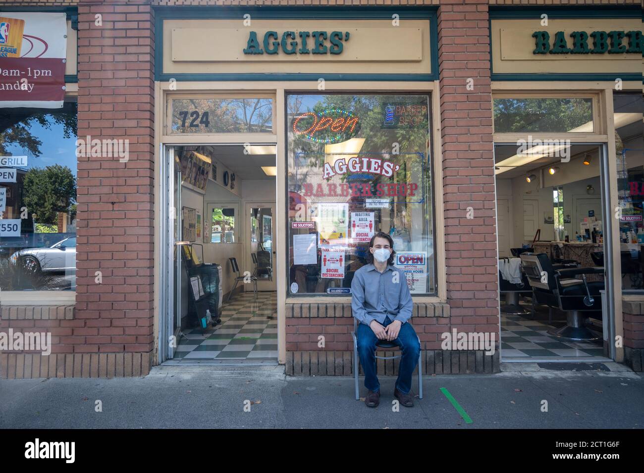 Davis, Californie, États-Unis. 19 septembre 2020. Un jeune homme est assis devant le salon de coiffure de cette ville universitaire en attendant une coupe de cheveux. Ce n'est que récemment que des barbiers ont été autorisés à opérer dans le comté de Yolo. Banque D'Images