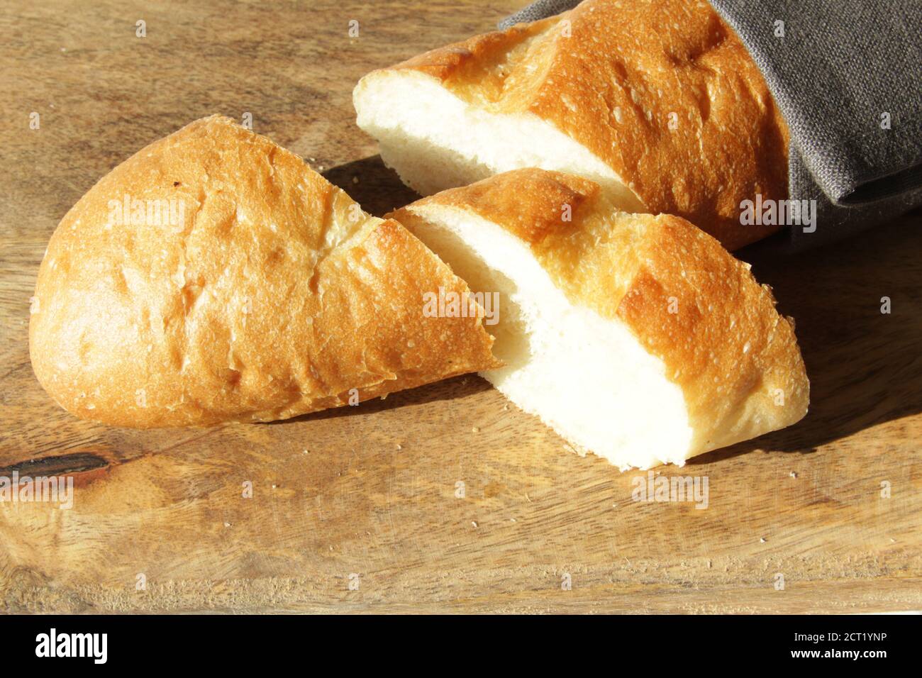 Baguette de pain doux frais français sur une planche à découper en bois. Plusieurs pièces de coupe sont couchés l'une à côté de l'autre. Banque D'Images