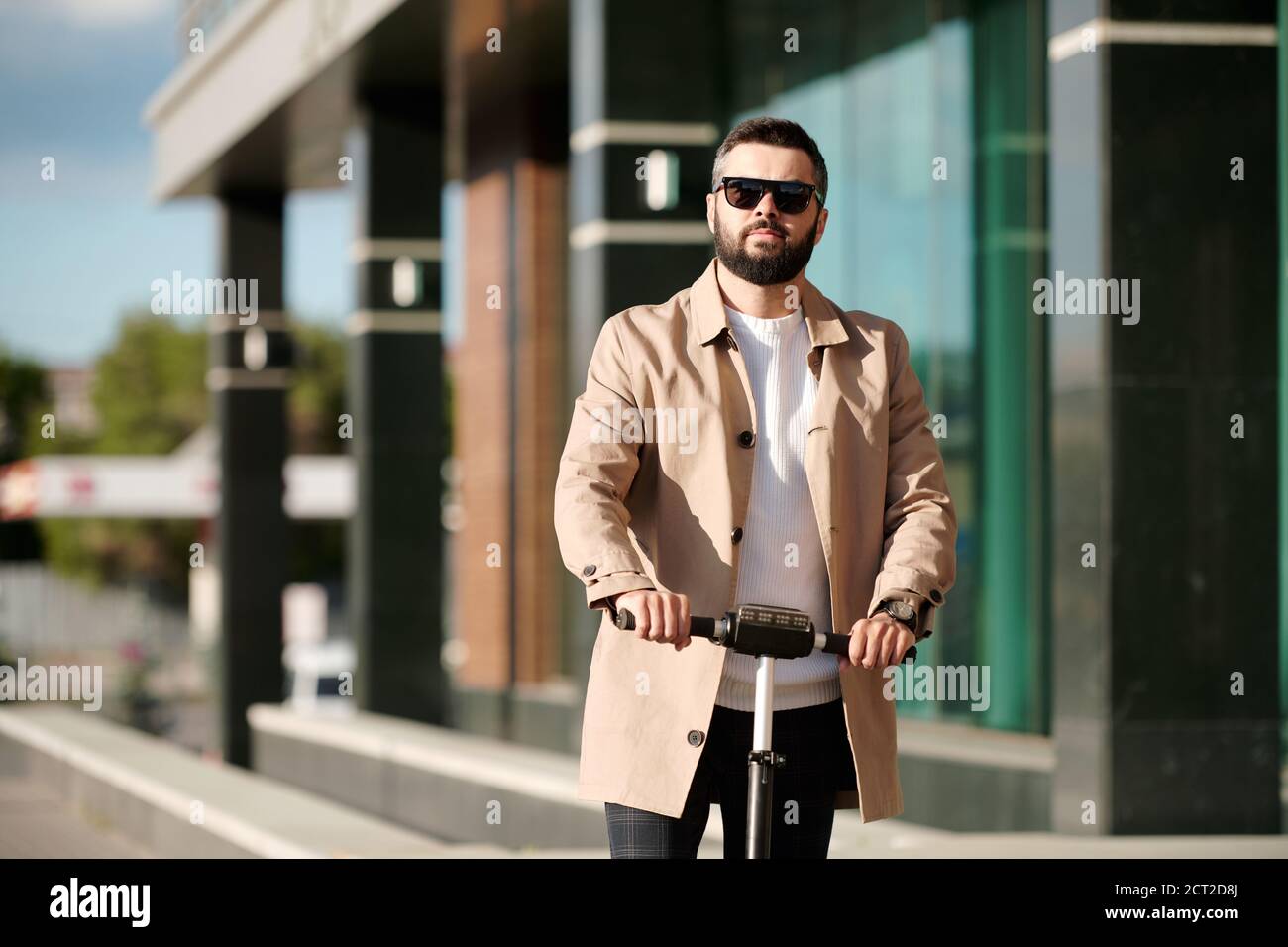 Homme d'affaires barbu sérieux en trenchcoat beige et lunettes de soleil à cheval Banque D'Images