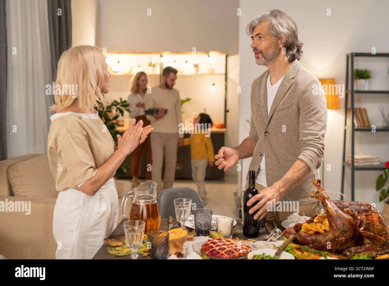 Homme barbu sérieux et mature tenant une bouteille de vin tout en parlant à sa femme Banque D'Images