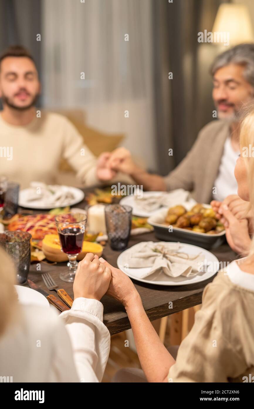 Famille contemporaine de quatre personnes priant par table festive servie dans séjour Banque D'Images