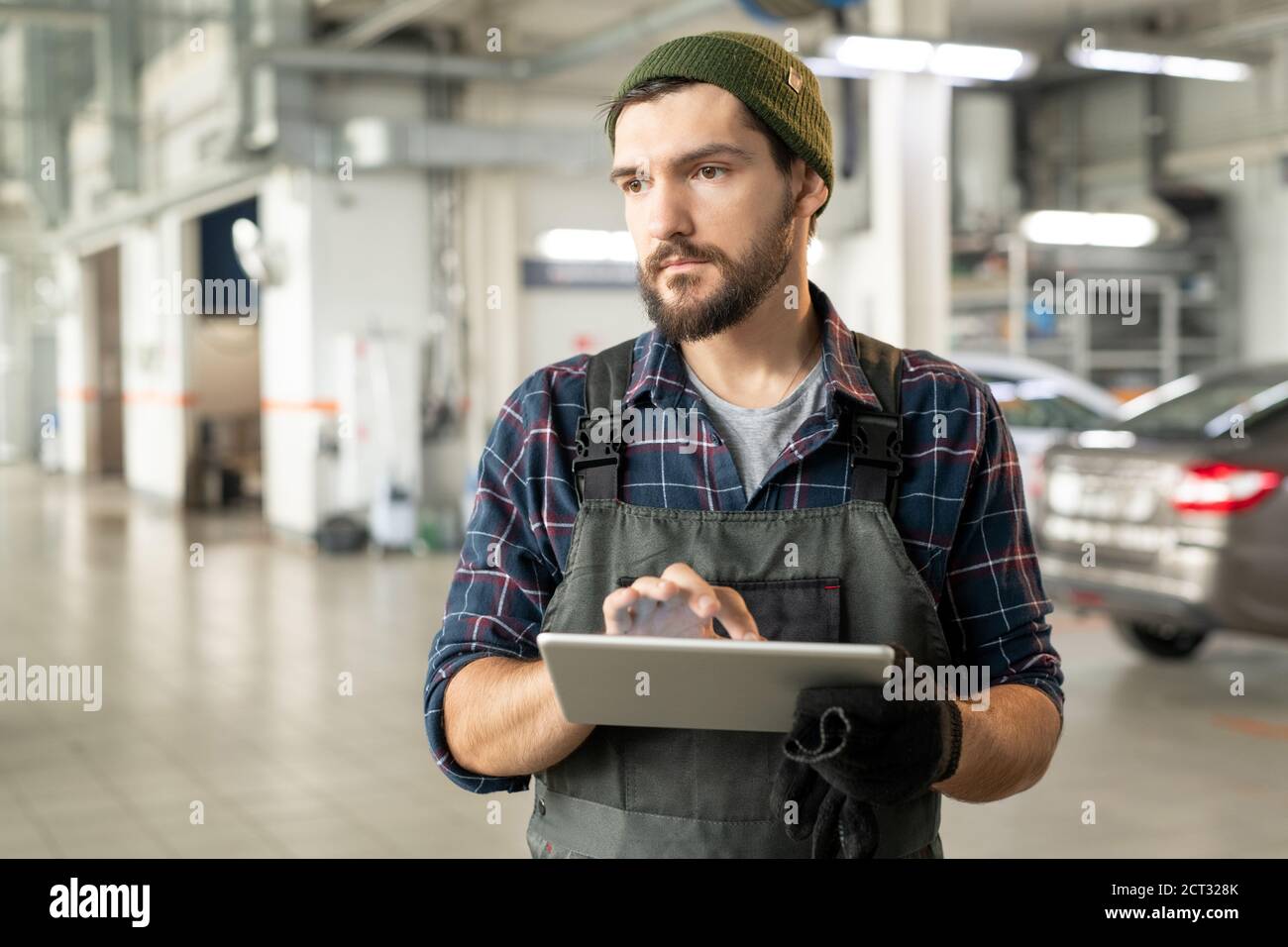 Jeune barbu technicien de service de voiture contemporain touchant l'affichage de tablette Banque D'Images