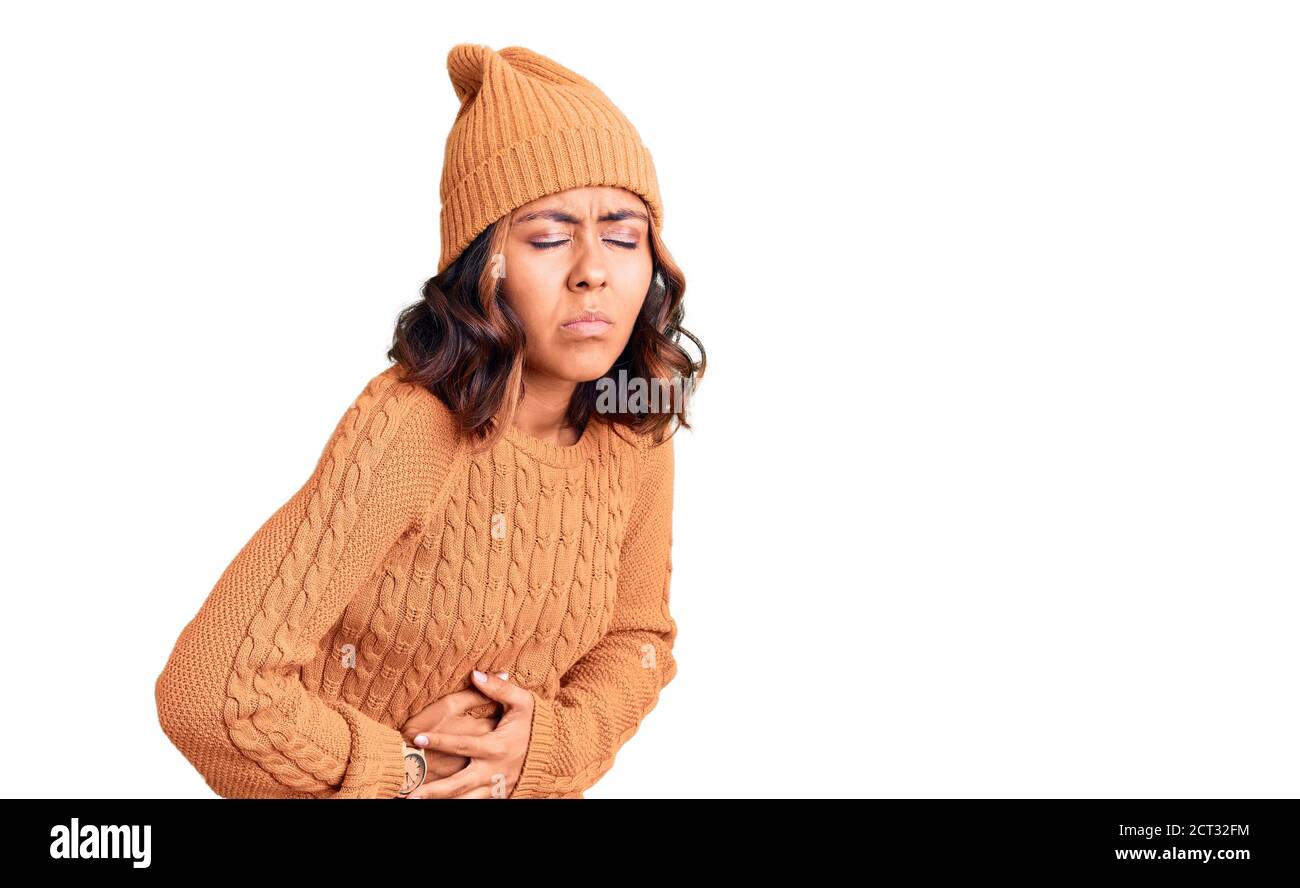 Jeune belle femme de race mixte portant un chandail en laine et un chapeau d'hiver avec main sur l'estomac parce que l'indigestion, la maladie douloureuse sentiment malaise. Ache co Banque D'Images