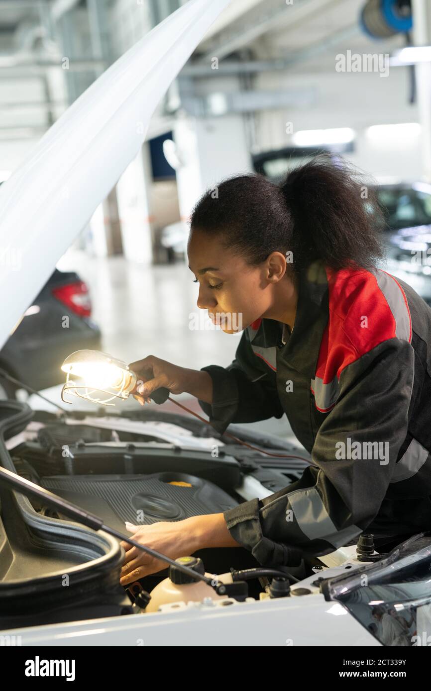 Jeune femme de course mixte avec lampe qui se plie au-dessus de la voiture ouverte capot Banque D'Images