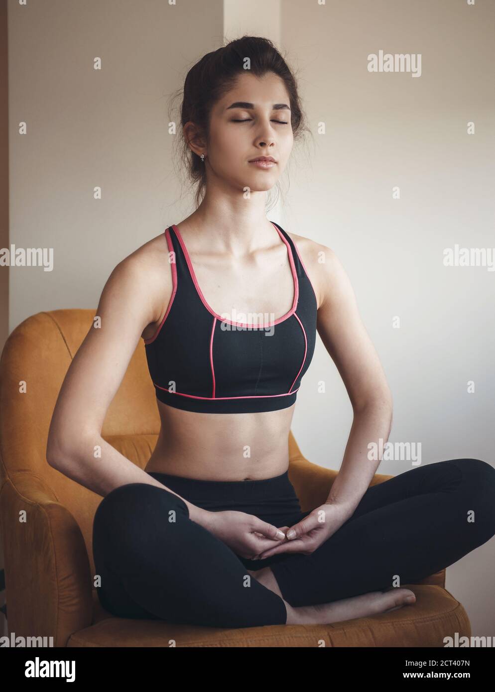 La femme caucasienne en vêtements de sport médite en étant assise sur un fauteuil avec les yeux fermés Banque D'Images