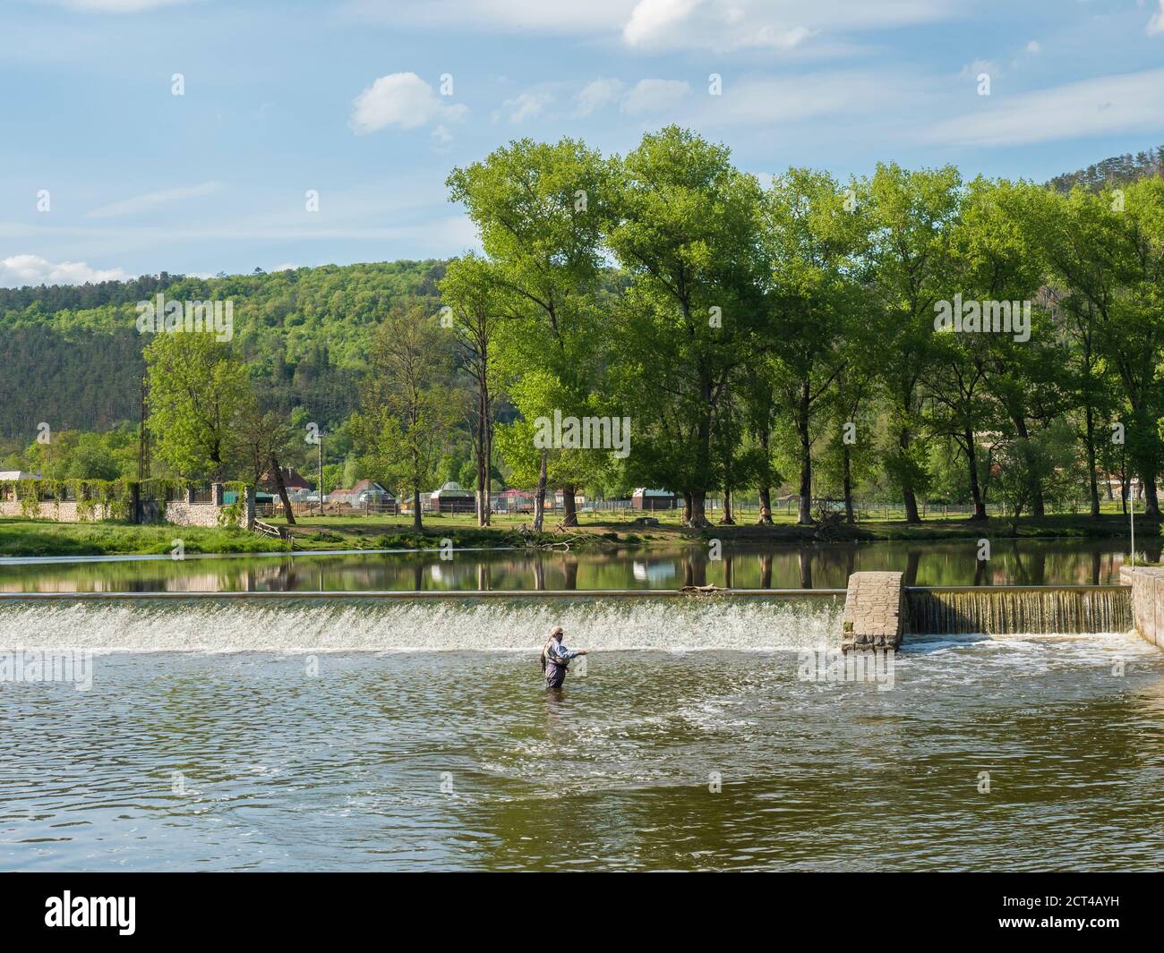 Weir sur la rivière Berounka dans le village de Zadni Treban avec pêcheur à la mouche debout dans le ruisseau et arbres verts luxuriants. Jour d'été ensoleillé, République tchèque Banque D'Images