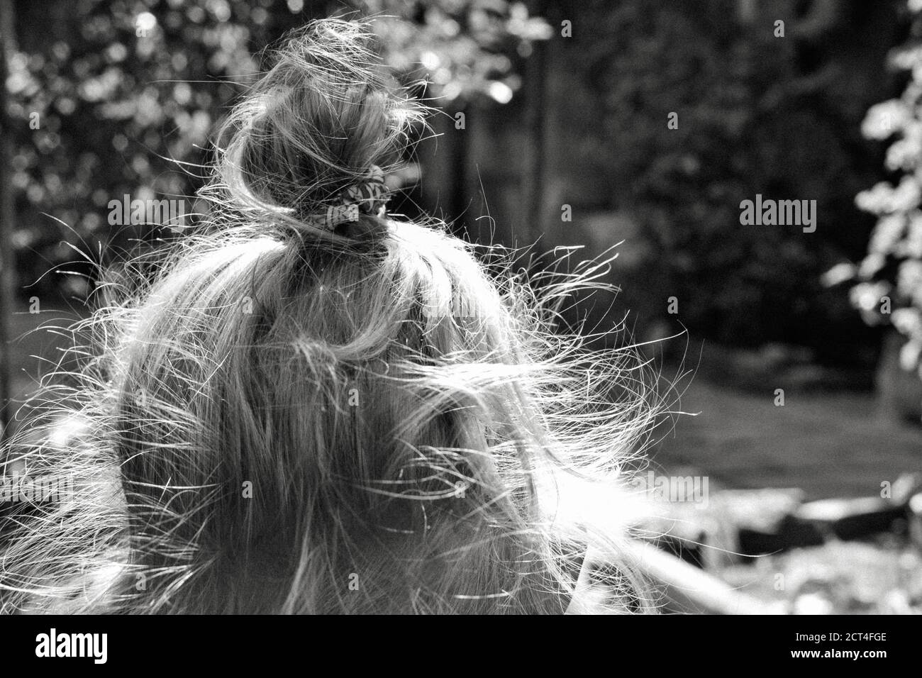 Petite fille avec de longs cheveux blonds bouclés sur le dos de sa tête. Fille avec de longues boucles brillantes dehors dans le jardin, jour ensoleillé d'été. Noir et Banque D'Images