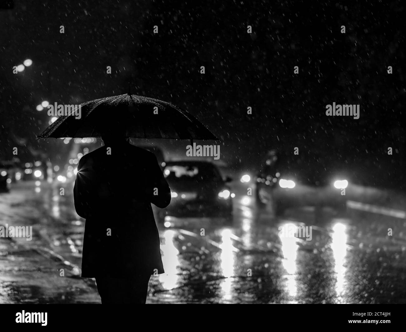 Silhouette d'un homme avec un parapluie dans le contre-jour des phares la nuit pendant une descente. Forte pluie dans la ville. Un piéton avec un parapluie Banque D'Images