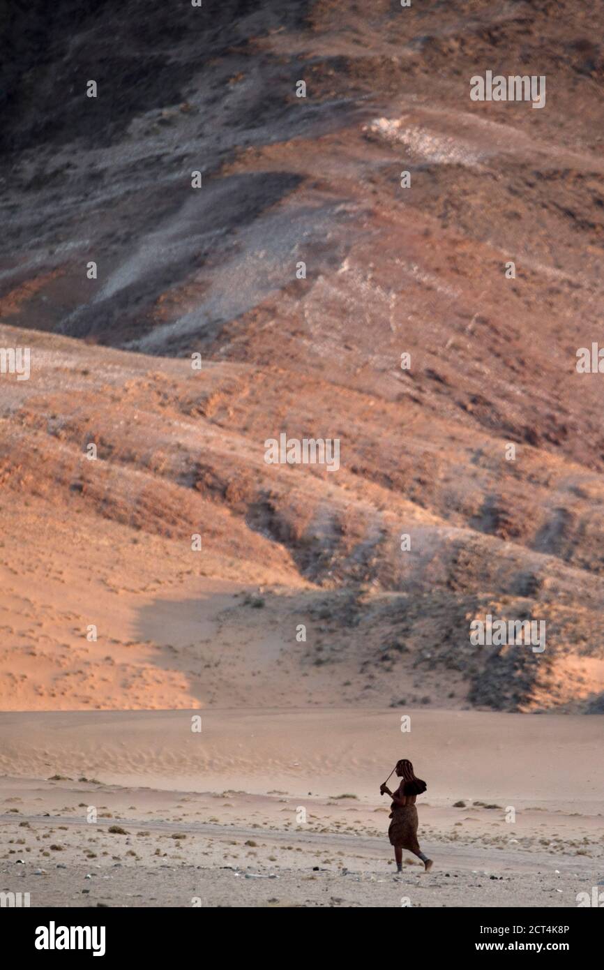 Une femme Himba marche dans la région aride qui entoure sa maison dans la région de Kunene en Namibie. Banque D'Images