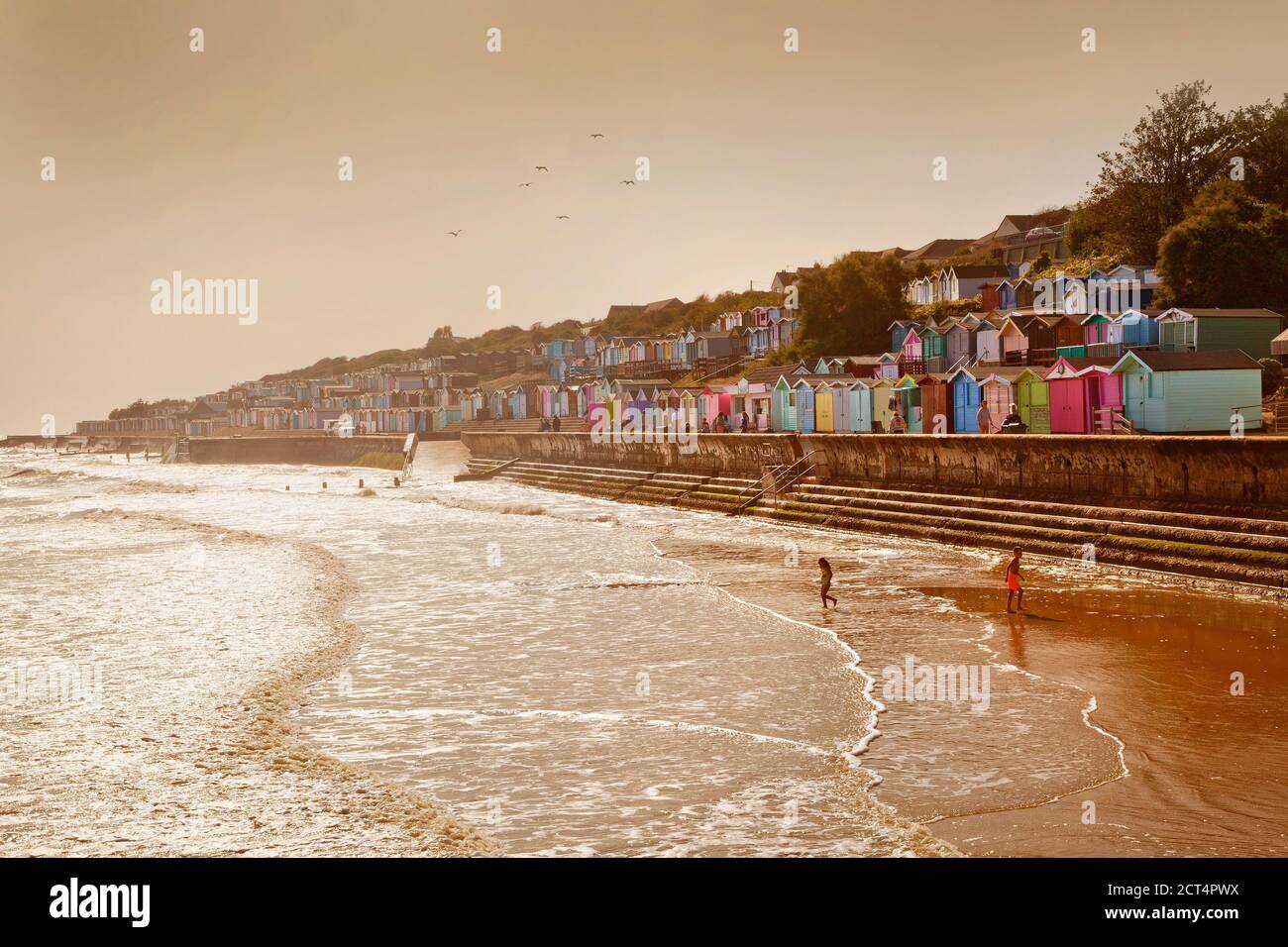 Walton-on-the-Naze, front de mer, Essex, Royaume-Uni. Des cabanes de plage colorées bordent la digue, lumière chaude le soir, plage avec deux enfants Banque D'Images